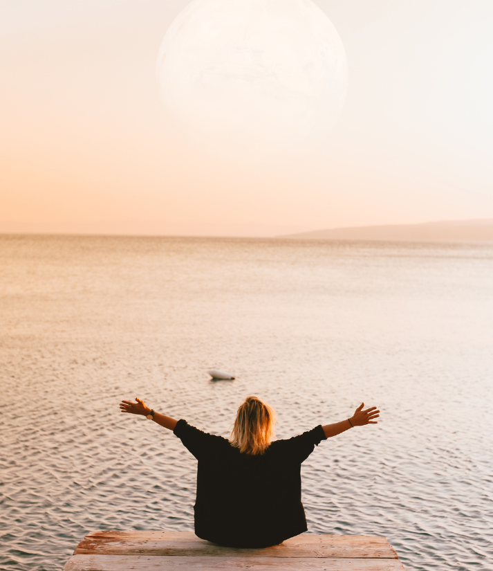 woman opening her arms towards sea and moon